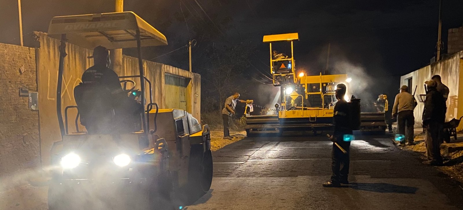 Rolo compactador e vibroacabadora em pavimentação noturna da Gidê